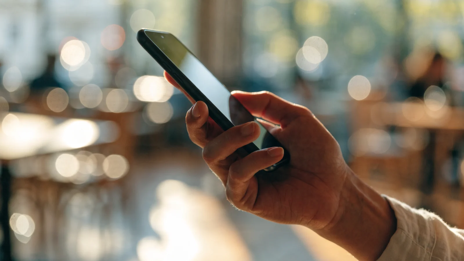 Hand holding a smartphone in a bright cafe while checking social media activity
