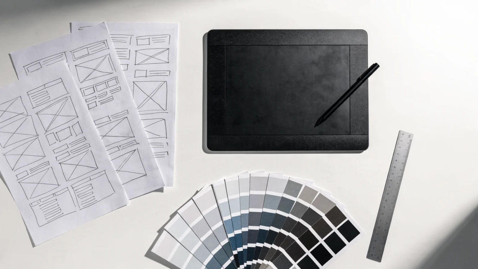 Designer desk with paper wireframe sketches, a graphics tablet and colour swatches